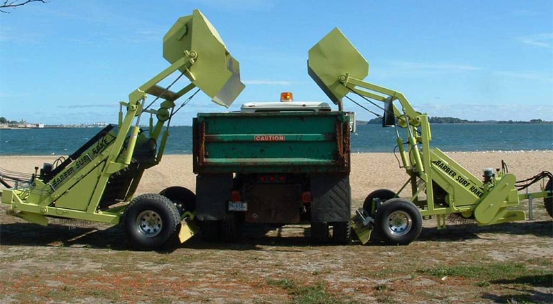 two high-dump surf rake beach cleaners dump into a truck on the beach